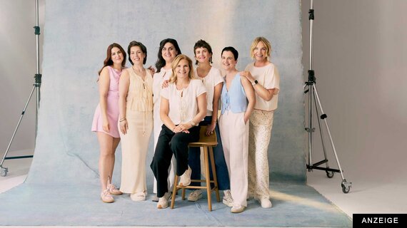 Sieben Frauen stehen lächelnd nebeneinander in einem Fotostudio.