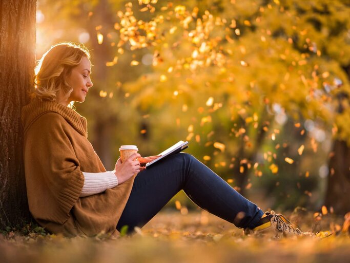 Person lehnt lesend am Baum | © Getty Images/BraunS