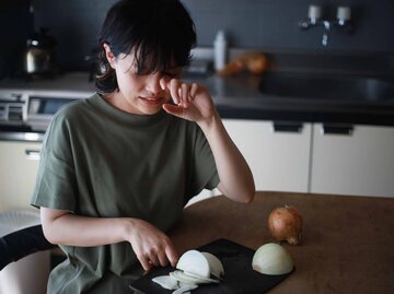 Frau weint beim Schneiden einer Zwiebel und reibt sich die Augen | © Adobe Stock/yamasan