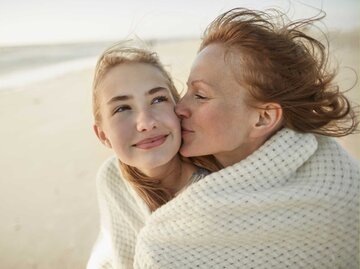 Mutter küsst Tochter am Strand auf die Wange | © Getty Images/Oliver Rossi