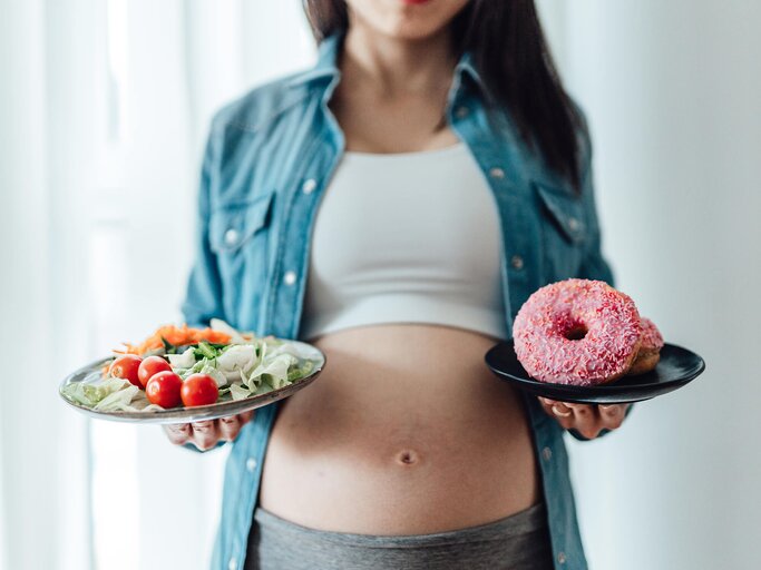 Schwangere Frau mit einem Teller Salat und einem Teller Donuts | © gettyimages.de | Oscar Wong