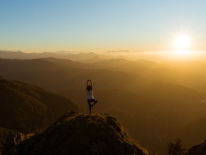 Frau macht Yoga auf einem Berg vor dem Sonnenuntergang | ©  Unsplash / Eneko Uruñuela