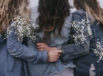 Drei Frauen in Jeansjacken stehen mit dem Rücken zur Kamera mit weißen Blumen in der Hand. | © Unsplash | Becca Tapert