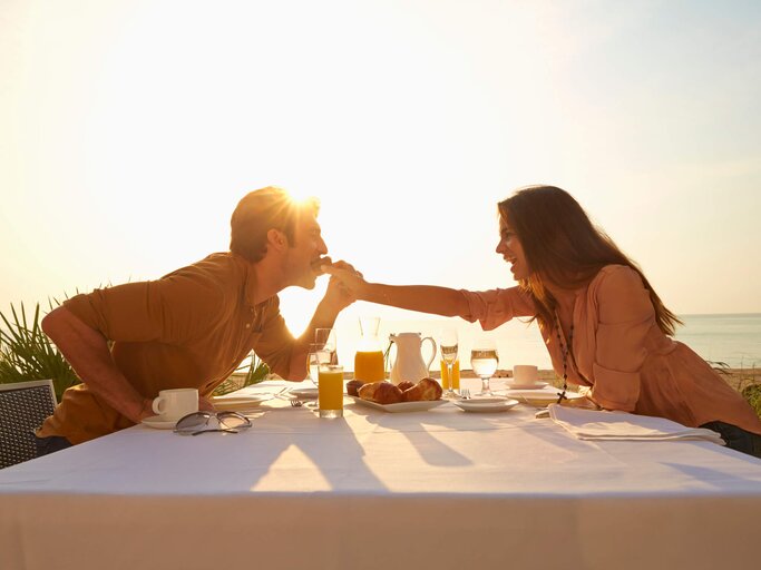 Pärchen in der Sonne isst zusammen am Tisch | © gettyimages.de |Colin Anderson Productions pty ltd