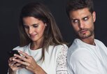 Frau sieht in ihr Handy, während der Mann daneben misstrauisch guckt | © gettyimages.de | PhotoAlto/Frederic Cirou