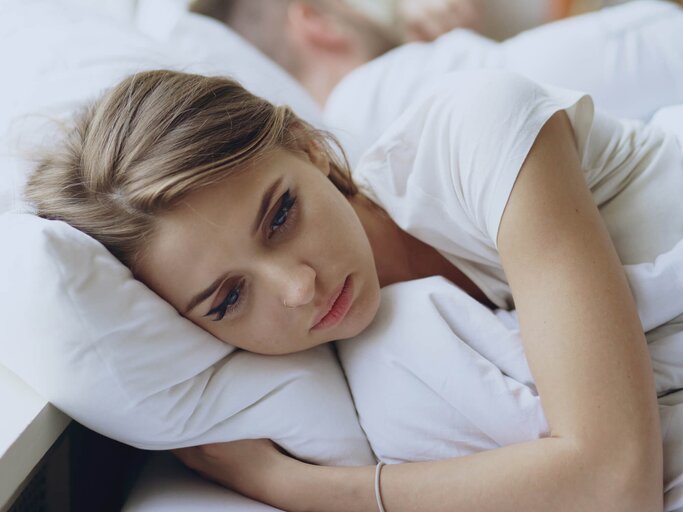 Junge Frau liegt traurig im Bett und hat Liebeskummer | © gettyimages.de / silverkblack