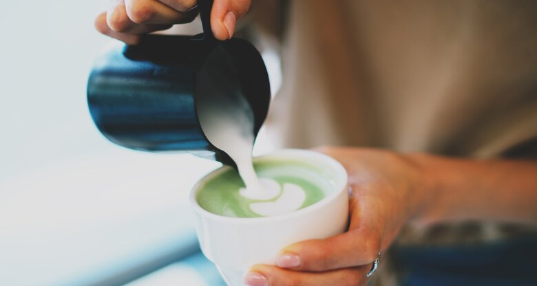 Frau gießt aufgeschäumte Milch in ihren Matcha Latte | © shutterstock / JKstock