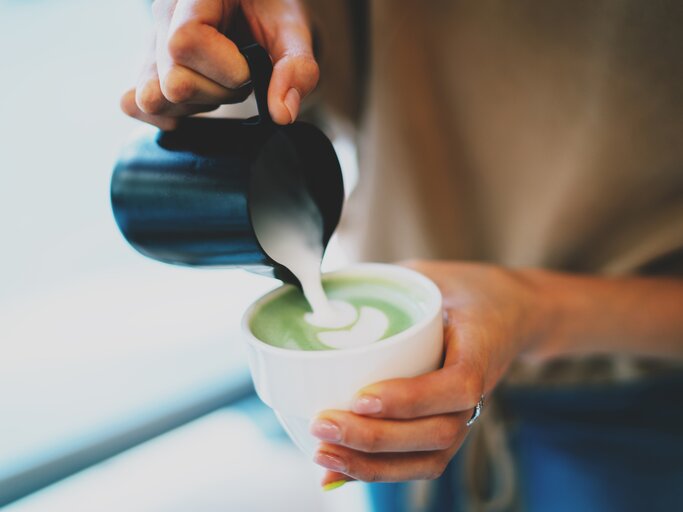 Frau gießt aufgeschäumte Milch in ihren Matcha Latte | © shutterstock / JKstock