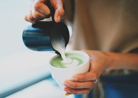 Frau gießt aufgeschäumte Milch in ihren Matcha Latte