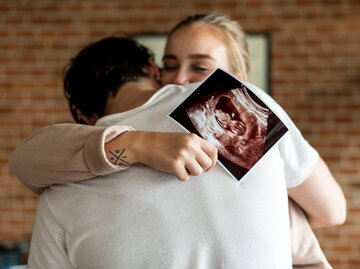 Frau umarmt Mann und zeigt Ultraschallbild | © gettyimages.de | Rawpixel