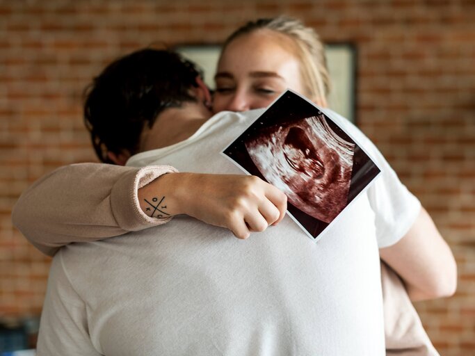 Frau umarmt Mann und zeigt Ultraschallbild | © gettyimages.de | Rawpixel