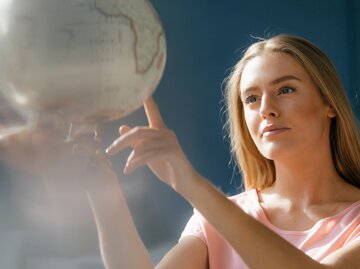 Junge Frau zeigt mit der Hand auf den Globus | © gettyimages.de | Westend61