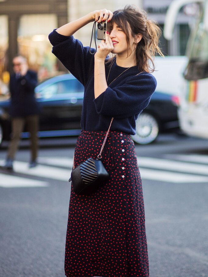 Street Style von Designerin Jeanne Damas mit marineblauem Kaschmirpullover, High Waist-Rock, Handtasche und Fotoapparat in Paris | © Getty Images | Christian Vierig