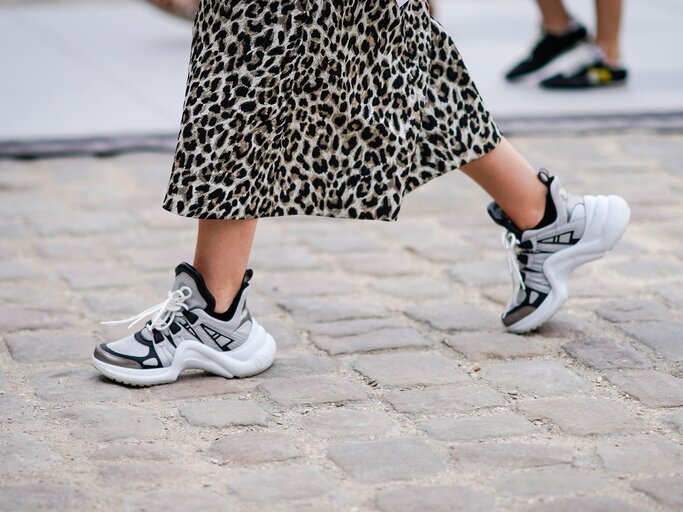 Detailaufnahme des Streetstyles einer Besucherin der Pariser Fashion Week in “Dad Sneakers” von Louis Vuitton zum Midirock mit Animal Print | © Getty Images / Edward Berthelot