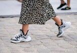 Detailaufnahme des Streetstyles einer Besucherin der Pariser Fashion Week in “Dad Sneakers” von Louis Vuitton zum Midirock mit Animal Print | © Getty Images / Edward Berthelot