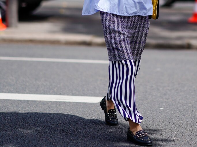 Detailaufnahme einer Besucherin der Menswear Fashion Week in Paris mit Print-Rock und Nieten-Loafern | © Getty Images / Edward Berthelot