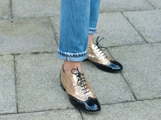 Detailaufnahme des Streetstyles der Influencerin Soraya Bakhtiar in gold-schwarzen Brogues von Chanel und Straight Leg-Jeans bei der Fashion Week in London | © Getty Images / Kirstin Sinclair
