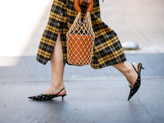 Detailaufnahme einer Besucherin in kariertem Rock und Kitten Heels mit Beuteltasche auf der Menswear Fashion Week in Mailand | © Getty Images / Christian Vierig