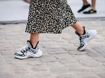 Detailaufnahme des Streetstyles einer Besucherin der Pariser Fashion Week in “Dad Sneakers” von Louis Vuitton zum Midirock mit Animal Print | © Getty Images / Edward Berthelot