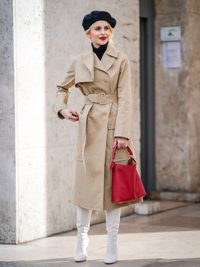 Street Style von Influencerin Caro Daur mit schwarzer Baskenmütze, beigem Trenchcoat, roter Handtasche und weißen Stiefeln in Mailand | © Getty Images | Edward Berthelot 