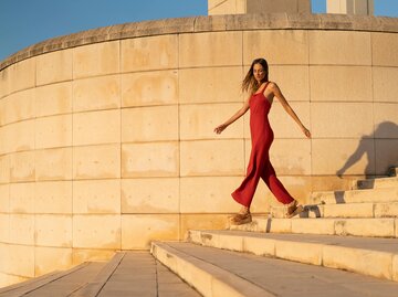 Frau in rotem Jumpsuit geht die Treppen hinunter | © Getty Images/Westend61