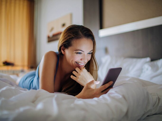 Frau liest SMS auf dem Bett liegend | © iStock | Geber86