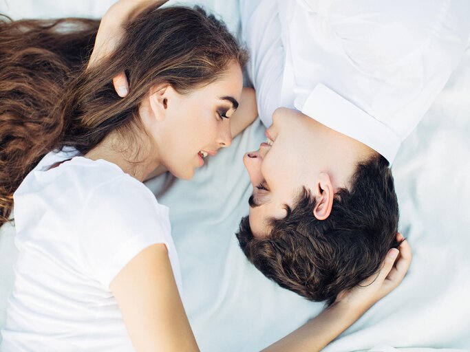 Paar liegt auf dem Bett und schaut sich an | © iStock | CoffeeAndMilk