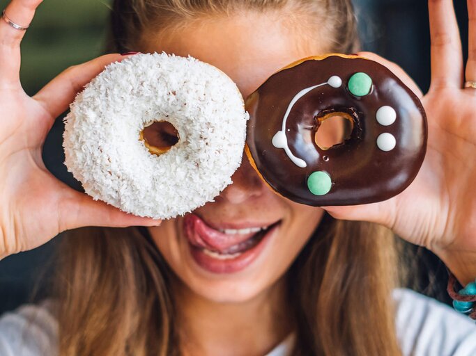 Frau hält sich zwei Donuts vor die Augen | © iStock | macarosha