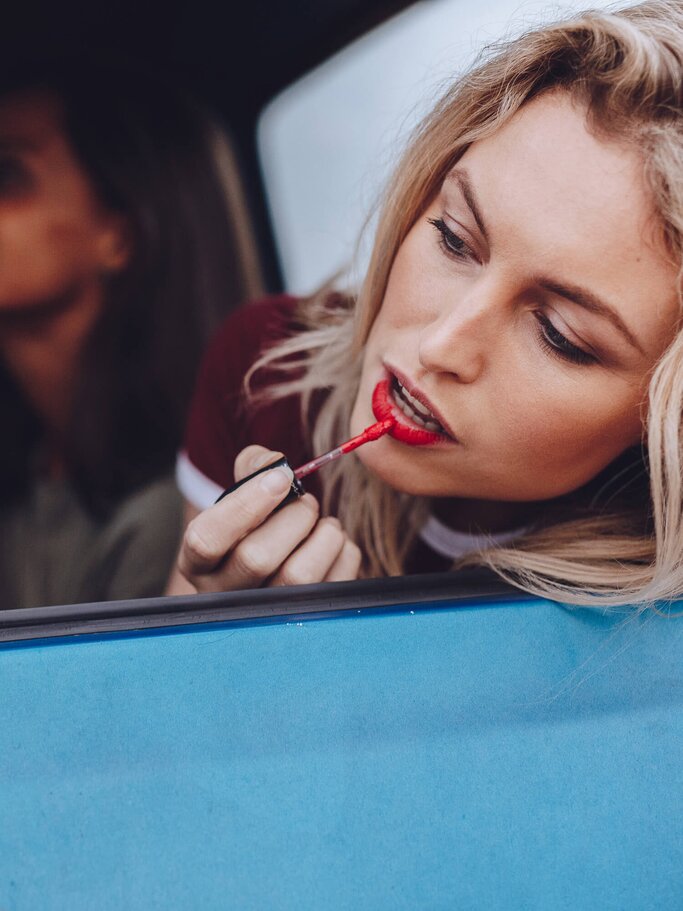 Frau schminkt sich im Autospiegel mit rotem Lippenstift | © iStock | jacoblund