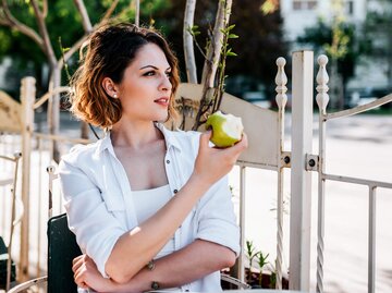Frau sitzt in einem Cafe und isst einen Apfel | © iStock | nortonrsx