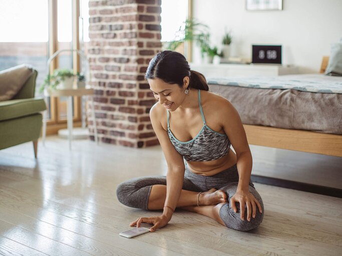 Frau in Sportkleidung bereitet sich auf geführte Meditation mit einer Smartphone-App vor | © iStock | svetikd