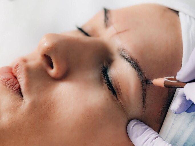 Nahaufnahme einer jungen Frau im Kosmetikstudio, der mit Kajalstift die Augenbrauen für Microblading aufgezeichnet werden | © iStock | microgen