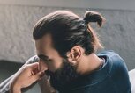 Ein Mann, der einen Man Bun und Vollbart trägt, sitzt auf einem Sessel. | © iStock | LightFieldStudios