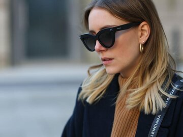 Junge Frau mit Sombre Hair in Aschblond mit hellblonden Spitzen trägt schwarze Sonnenbrille, einen beigen Pullover, einen schwarzen Mantel und eine Balenciaga Umhängetasche | © Getty Images | Jeremy Moeller 