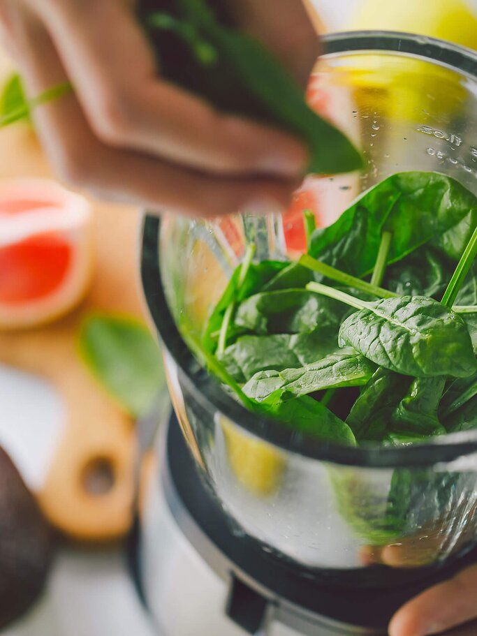 Frau gibt Spinatblätter in einen Mixer für einen Smoothie | © iStock | nerudol