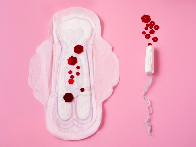 Monatsbinde und Tampon liegen mit roten Pailletten in verschiedenen Größen auf rosa Oberfläche | © iStock | Alina Indienko