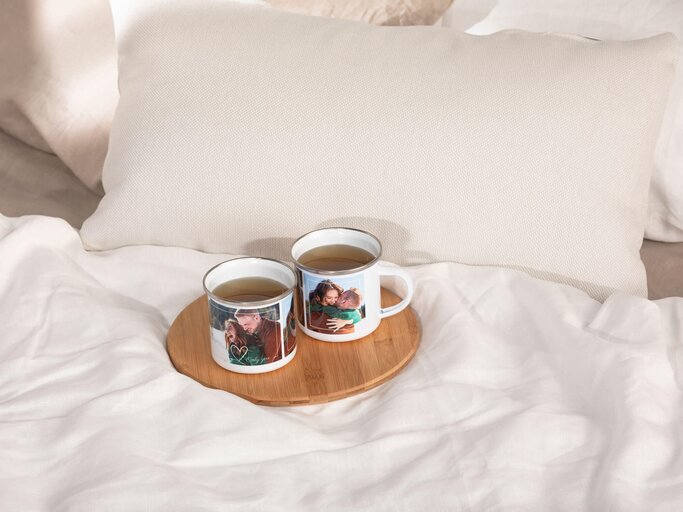 Zwei personalisierte Emaille Becher mit Fotos von einem Paar stehen auf dem Bett. | © PR