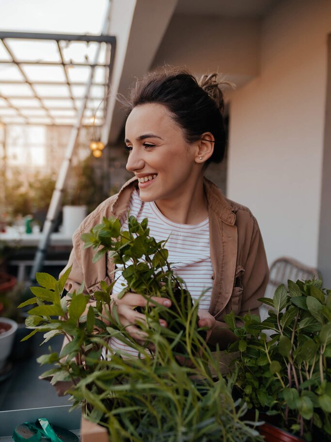 Junge Frau arrangiert Blumen und Pflanzen auf ihrem Balkon | © iStock | AleksandarNakic