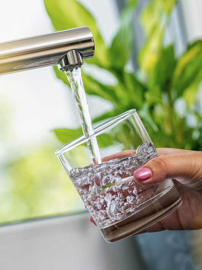 Frau Hand hält ein Glas, um es mit Wasser aus dem Hahn zu füllen | © iStock | rclassenlayouts