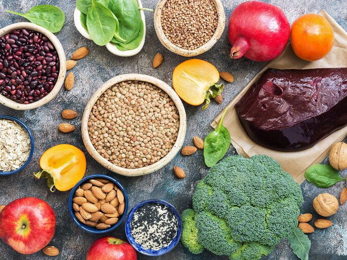 Auf einem Tisch liegen eisenhaltige Lebensmittel, darunter Leber, Linsen, Brokkoli, Bohnen und Spinat | © iStock | Yulia Gusterina