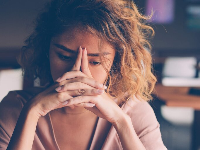 Junge Frau hält sich den Kopf, ist niedergeschlagen und erschöpft | © iStock | MangoStar_Studio