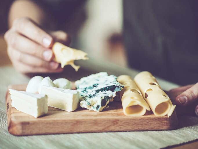 Frau richtet eine Platte mit unterschiedlichem Käse an | © iStock | Eva-Katalin