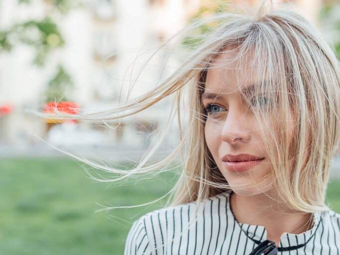 Junge blonde Frau steht mit fliegenden Haaren im Wind | © iStock | Ivan Pantic