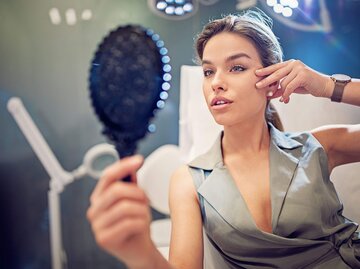 Frau in einer Arztpraxis schaut sich im Spiegel an wegen einer Schönheits-OP | © iStock | praetorianphoto