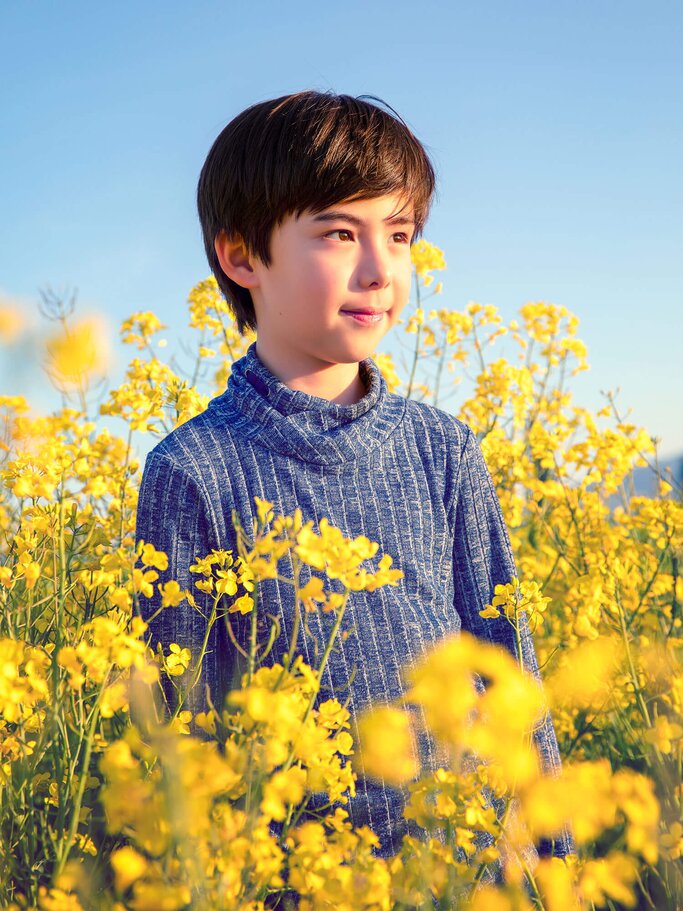 Glücklicher Junge auf einem Feld von gelben Blumen bei Sonnenuntergang | © iStock | Benoitbruchez