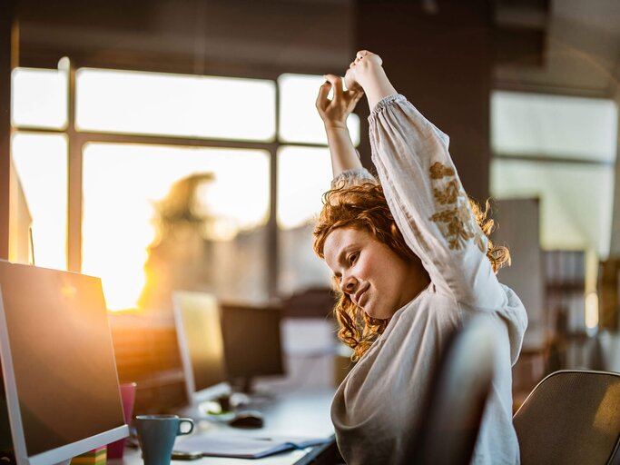 Frau streckt sich bei Sonnenuntergang an ihrem Laptop | © iStock | skynesher