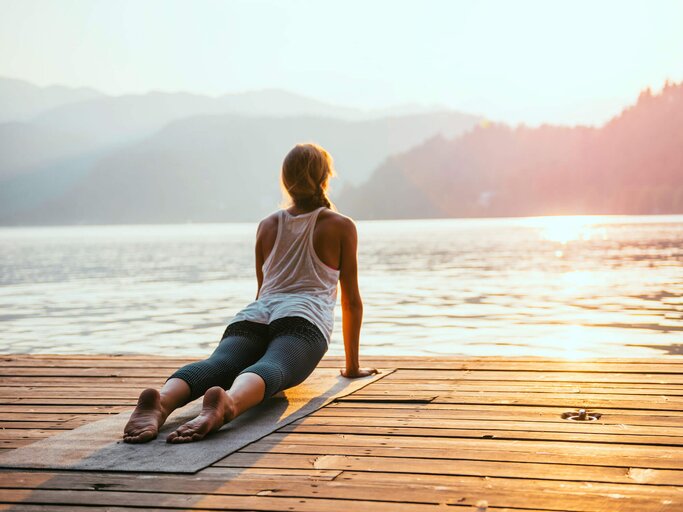 Junge Frau auf einem Steg übt den Sonnengruß. | © iStock | microgen