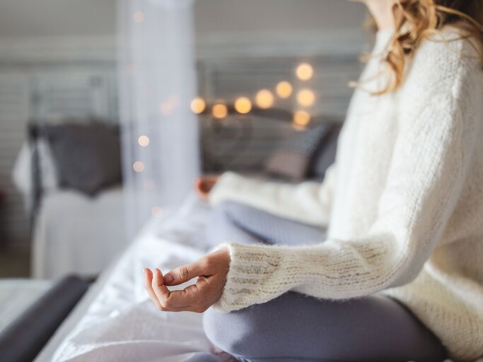 Junge Frau sitzt in einer entspannten Yoga-Pose auf dem Bett | © iStock | Jasmina007