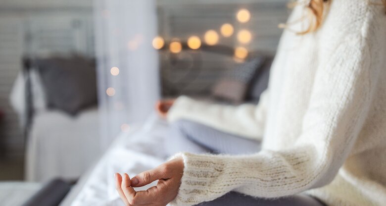 Junge Frau sitzt in einer entspannten Yoga-Pose auf dem Bett | © iStock | Jasmina007