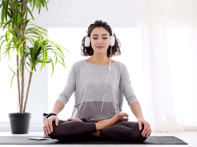 Moderne Frau mit Kopfhörern sitzt in Yoga-Botus-Haltung und meditiert | © iStock | monstArrr_